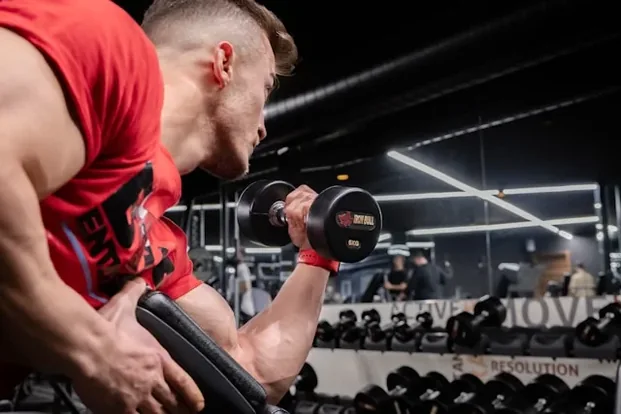 Mand i rød tanktop der laver bicepscurl med håndvægt i et motionscenter
